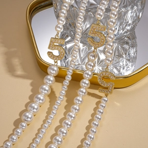 Detailed close-up of faux pearl strand necklace with gold number five pendant charms