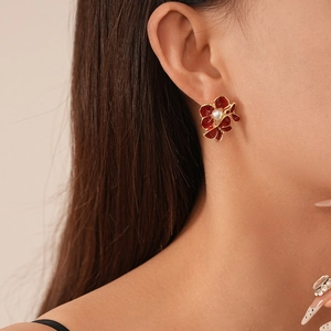 Close-up of vintage red flower earring with gold edges and pearl on woman ear