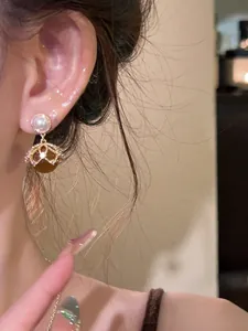 Detail of 18K gold-plated drop earring with pearl and brown stone on ear model