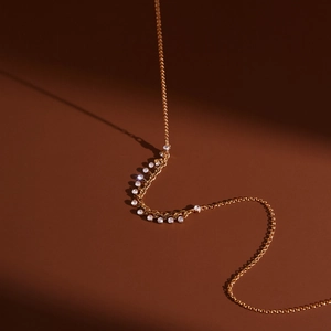 Dettaglio della collana placcata oro 18K con nappe di zirconi rotondi su sfondo rosso intenso
