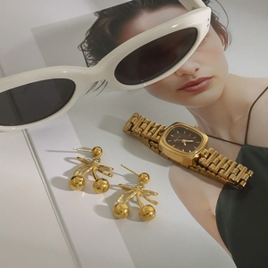 Goldene Kirschohrringe mit quadratischer Vintage-Uhr auf einem Modemagazin