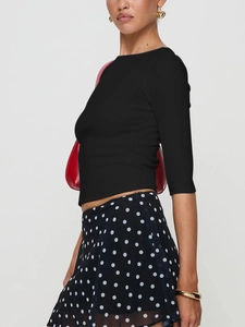 Detail of black slim fit knit top with ribbed texture and elegant gold heart earrings