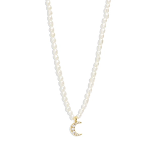 Macro detail of gold crescent moon pendant with crystals on white pearl necklace