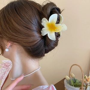 Detail showing a white and yellow frangipani flower hair claw clip in a hair updo