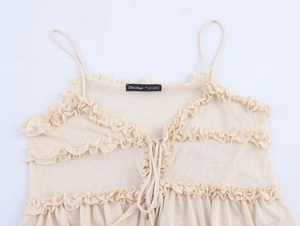 Detail of beige ruffled knit top with lace-up shoulder straps and ribbed texture