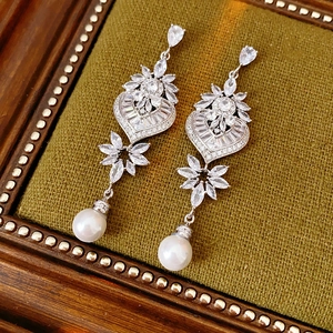 Close-up of silver heart and flower earrings with crystals and pearl on green velvet