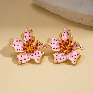 Pink enamel flower earrings with gold edges and red centers on a textured stone surface