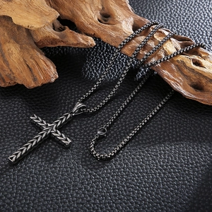 Detail of black box chain necklace with textured cross pendant on natural wood background