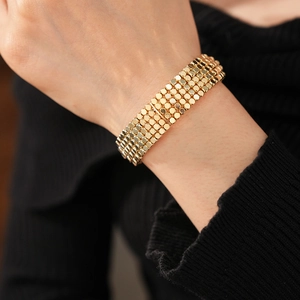 Gros plan d'un bracelet multicouche en perles dorées porté au poignet sur fond de tricot noir