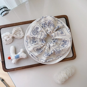 Close-up of floral print cotton scrunchie in beige and blue on a white ceramic plate