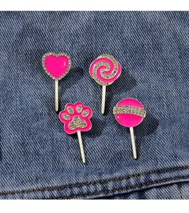 Close-up of pink heart, lollipop, and paw-shaped rhinestone brooches on blue denim fabric