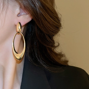 Polished gold oval hollow pendant earrings worn by a model in a formal professional style