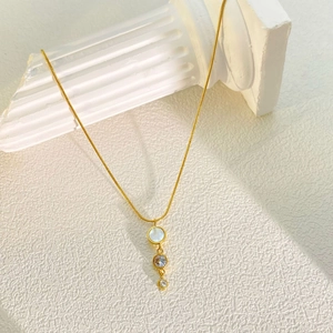 Macro detail of golden stainless steel necklace with white shell inlay and zircon drop