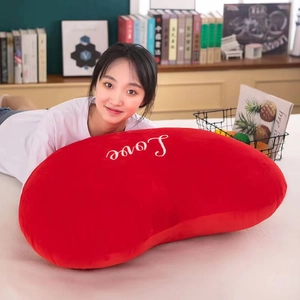 Close-up of a large red plush heart pillow with white Love embroidery in a cozy bedroom