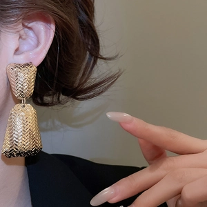 Close-up of golden metal earrings featuring a textured woven pattern in a trapezoid shape