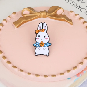 Close-up of cute white rabbit enamel pin with blue floral dress and orange bow accessory