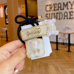 Detail of golden hair clip and elastic tie set with white pearlescent bear and GoodLuck text