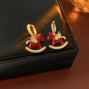 Macro shot of red rocking horse earrings with gold wings on a black leather box