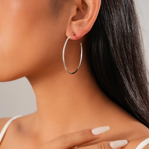 Close-up of a woman wearing large polished silver hoop earrings with a shiny finish