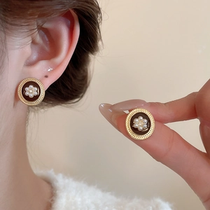 Detailed close-up of retro gold-plated round earrings with black enamel and pearl flower