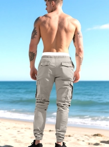 Men's light grey cargo pants with multiple pockets shown in an outdoor beach setting