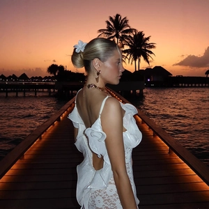 Robe longue blanche en dentelle dos nu avec volants devant un coucher de soleil à la plage