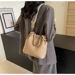 Detail of khaki leather bucket bag with geometric patterned wide strap on model