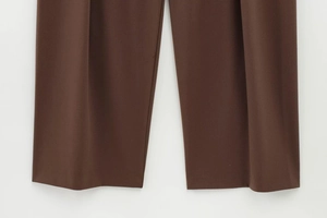 Detail of dark brown straight leg trousers with a refined drape and smooth fabric texture