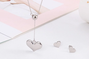 Close-up of silver heart necklace and matching stud earrings set on a white surface