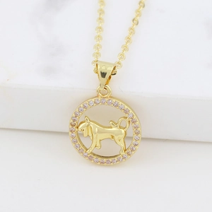 Close-up of gold zodiac Taurus pendant with pink crystal on white marble