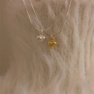 Detailed view of 3D gold and silver heart necklaces on a soft white plush background