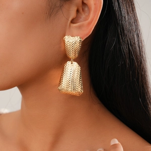 Detail of gold metal earrings with woven texture and geometric drop design on model