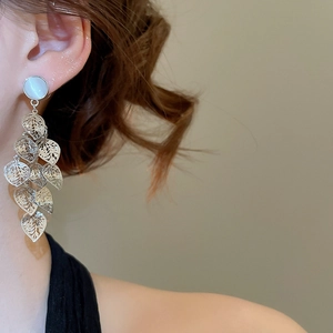 Silver openwork leaf tassel earrings with white opal stone shown on model's ear