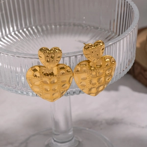 Detailed close-up of golden heart earrings with hammered texture on a glass rim
