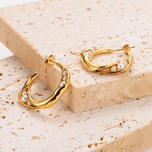 Macro shot of gold C-shaped twisted pearl earrings on a light textured stone background