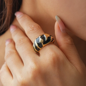 Detail of wide gold-plated ring with black enamel texture worn on the index finger