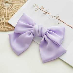 Close-up of a large purple satin bow hair clip on a minimalist decorative background