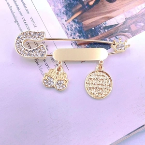 Close-up of golden brooch pin featuring hamsa hand, crown, and coin charms with rhinestones