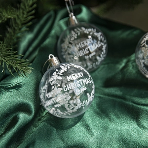 Clear acrylic Christmas ornament with white Merry Christmas lettering on green silk fabric