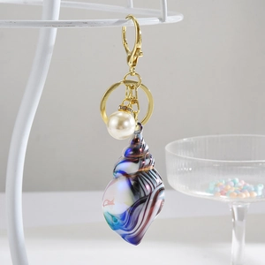 Exquisite colorful conch shell keychain with pearl and golden ring on display stand