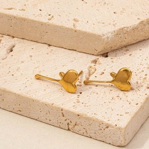 Close-up of minimalist golden heart stud earrings resting on a textured beige stone base