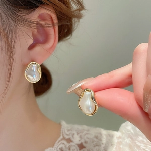 Detail of irregular baroque pearl earrings with gold bezel shown on model and hand