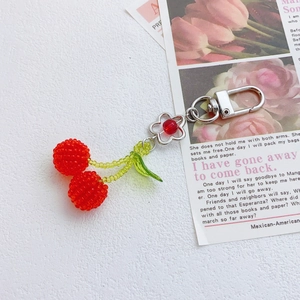 Detail showing crystal beaded cherry keychain with silver flower clasp on textured surface