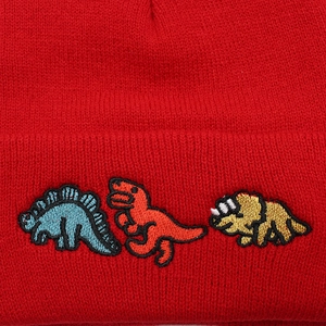 Nahaufnahme von drei Dinosaurier-Stickereien auf einem roten Beanie aus Strickmaterial