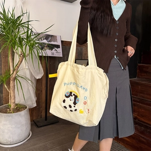 Detail of canvas tote bag with Puppy embroidery and drawstring closure on shoulder