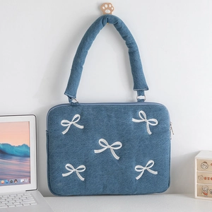Détail de la sacoche pour ordinateur en denim bleu avec broderie de papillon blanc au mur