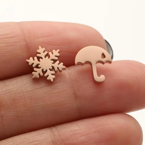 Rose gold snowflake and umbrella mismatched stud earrings held between fingers