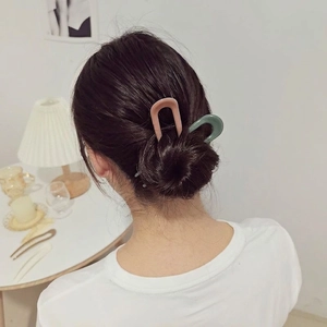 U-shaped hair pins in matte pink and green, shown on a bun in a home setting