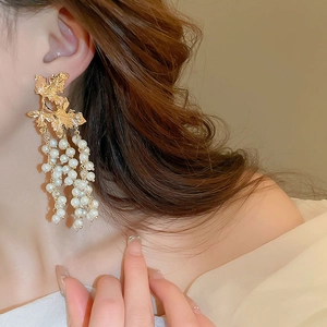 Elegant gold maple leaf earrings with white imitation pearl tassels worn by a model