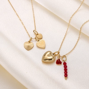 Detail of vintage heart charms and red beads on gold stainless steel necklaces